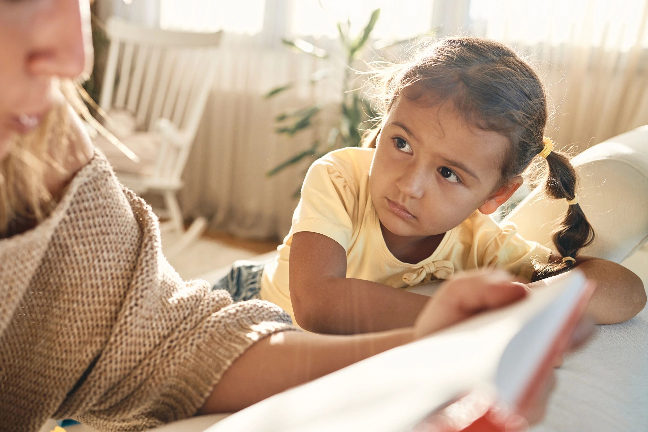 Mother reading a book to her young attentive daughter at home