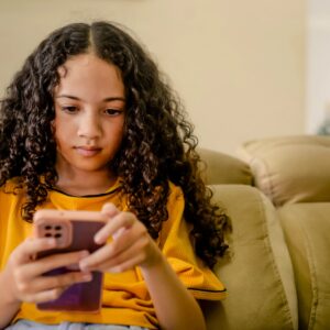 A girl concentrating on her cell phone, wearing a yellow shirt.