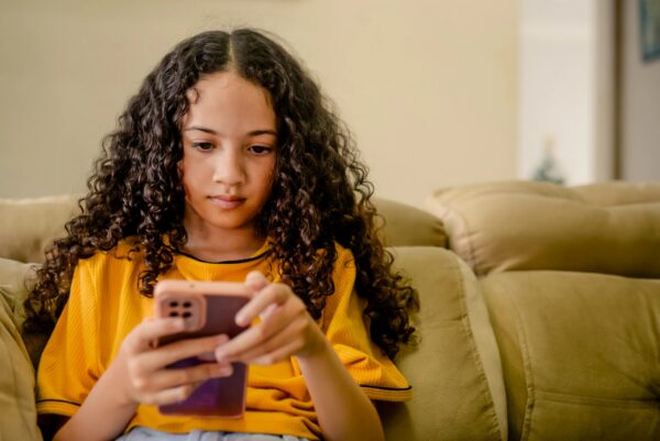 A girl concentrating on her cell phone, wearing a yellow shirt.